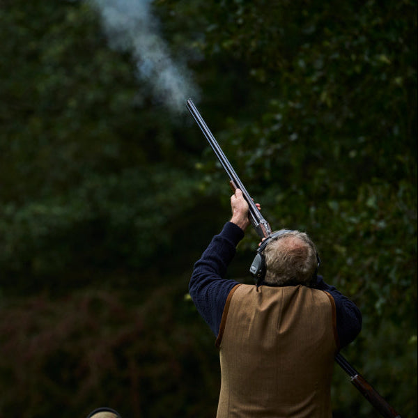 Person holding a shotgun with smoke in a forest setting